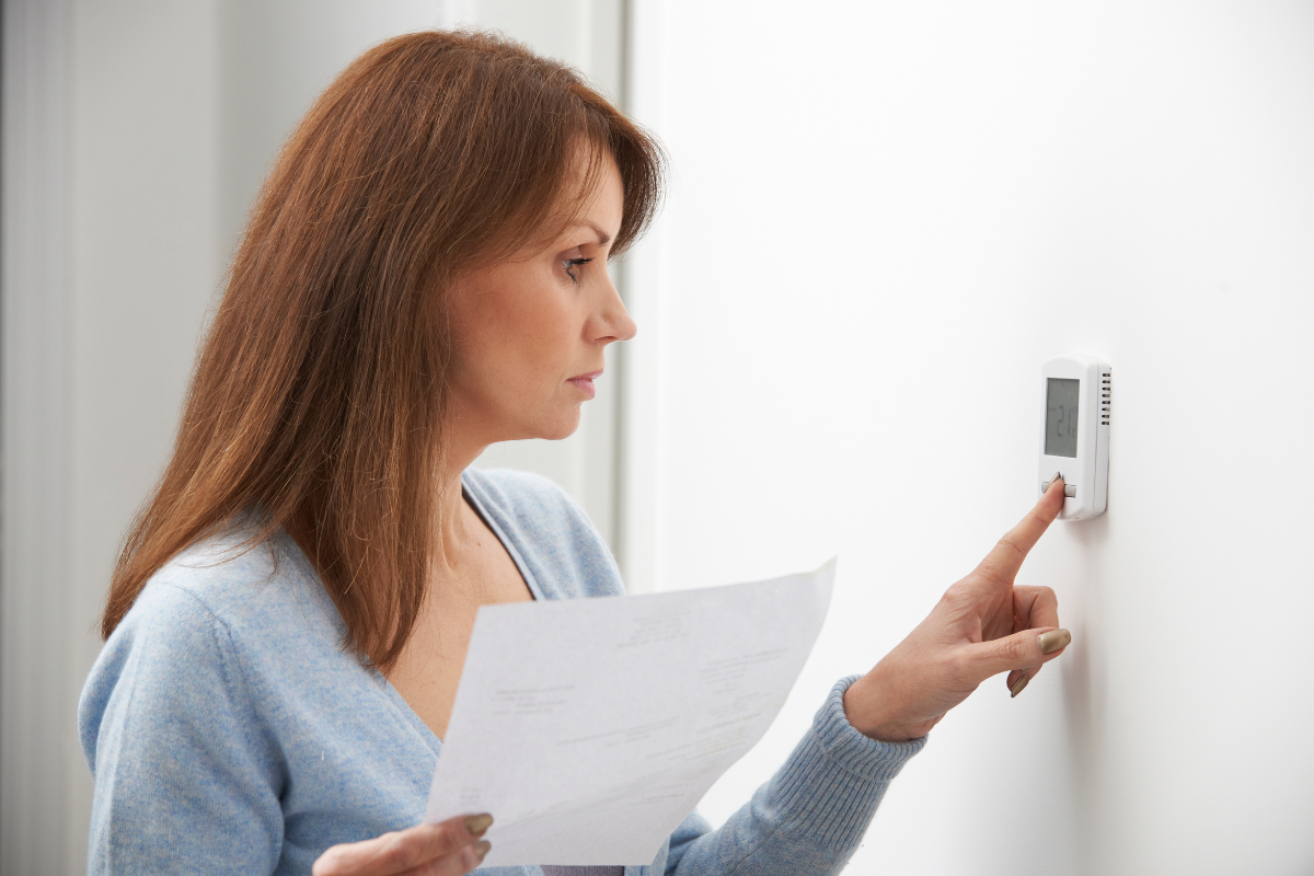 woman-holding-utility-bill-while-adjusting-thermostat